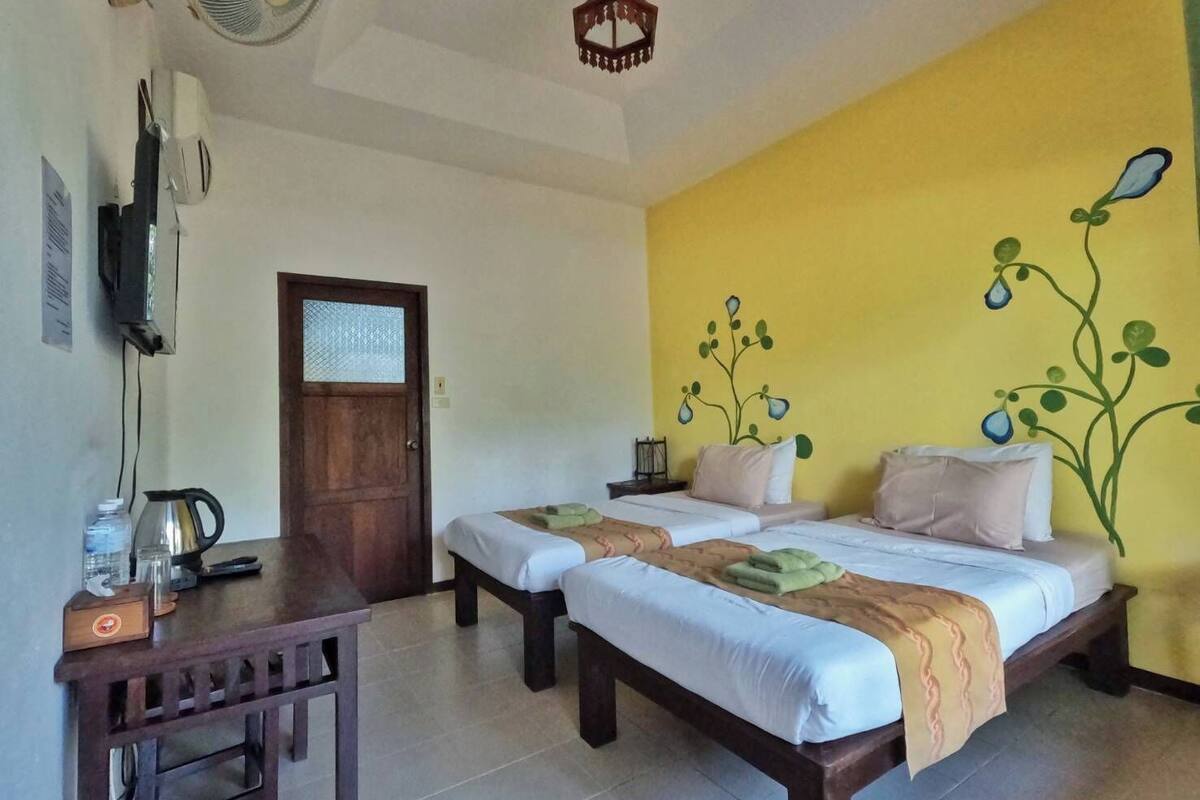 A room with two beds, a desk, a kettle, and a wall with a plant mural.