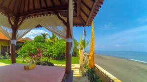 Um gazebo à beira-mar com uma cama, vista para o oceano e plantas tropicais.