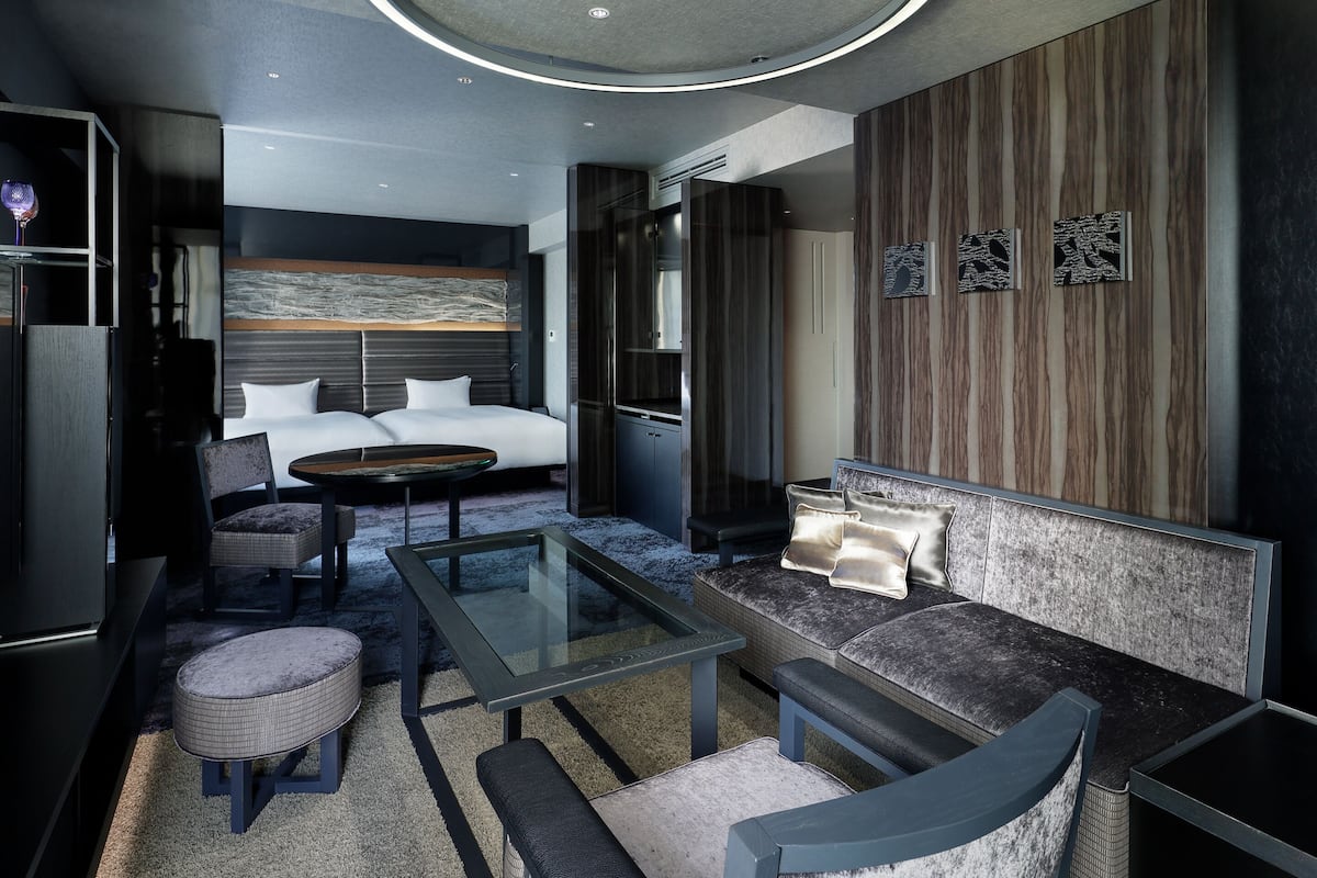 Quarto de hotel moderno com cama, sofá, mesa de centro e área de estar.