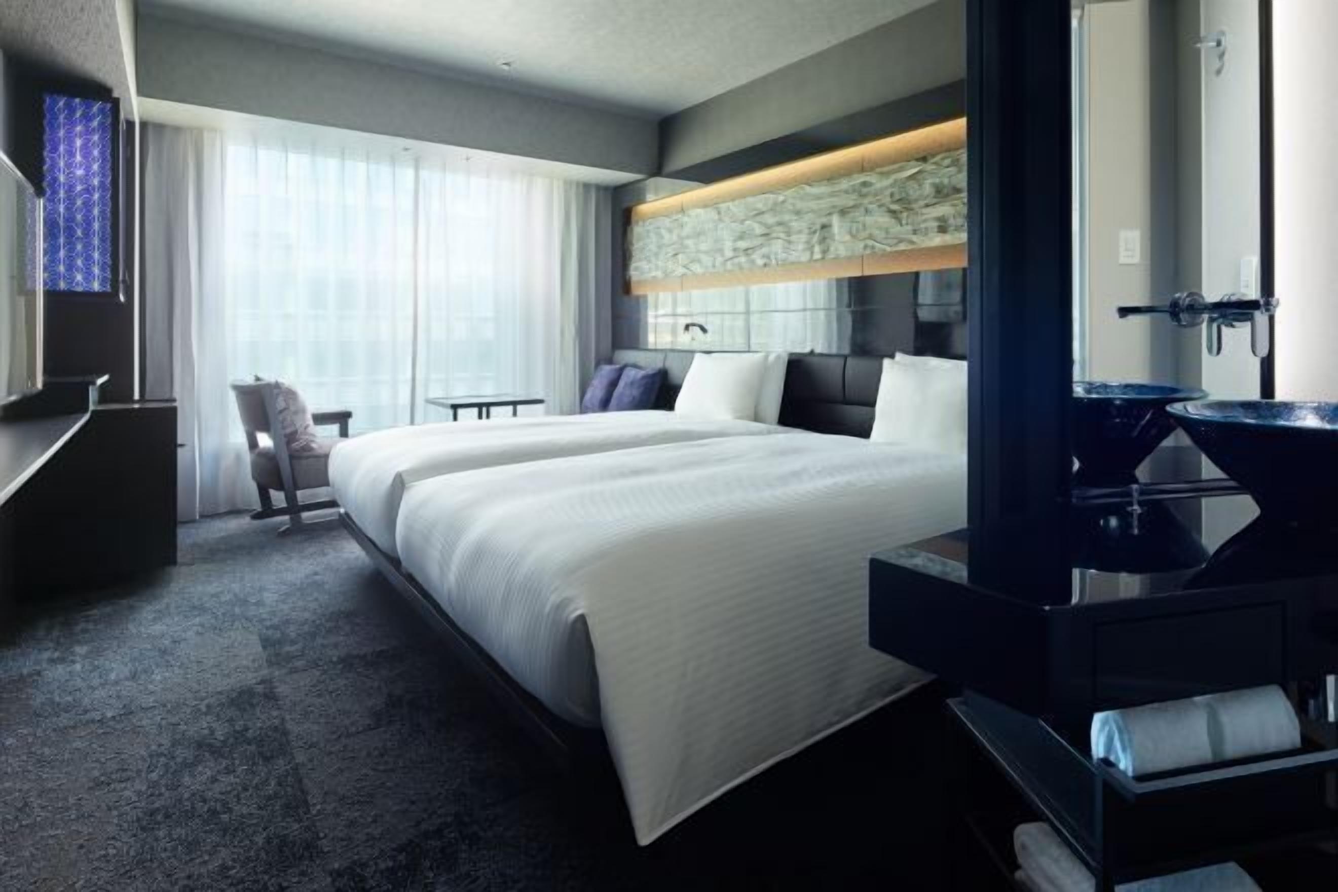 Une chambre d’hôtel avec un grand lit, un bureau, une chaise, une coiffeuse avec un miroir et une fenêtre avec des rideaux.