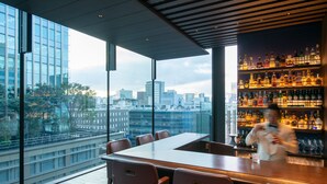 Eine moderne Bar mit Blick auf die Stadt, ausgestattet mit einem langen Tisch und Stühlen sowie einer gut sortierten Spirituosenregal.