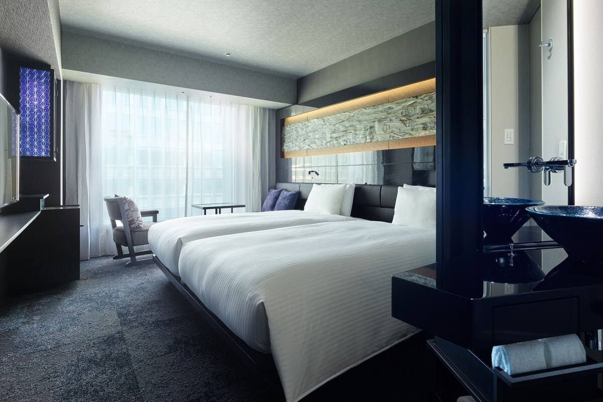 Quarto de hotel com uma cama grande, uma escrivaninha, uma cadeira, um banheiro com espelho e uma janela com cortinas.