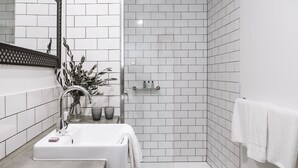 Un baño moderno con lavamanos, espejo y zona de ducha blancos.