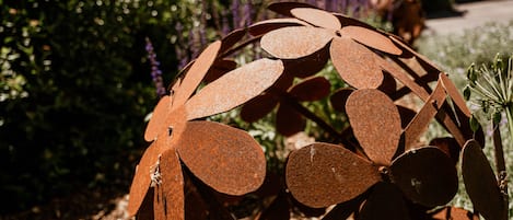 Una escultura de metal en un jardín con plantas y un edificio al fondo.