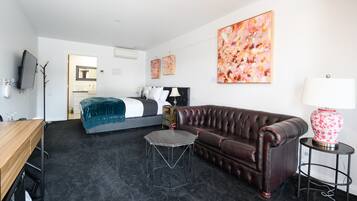 A modern hotel room with a bed, a leather sofa, a small table, and a TV.
