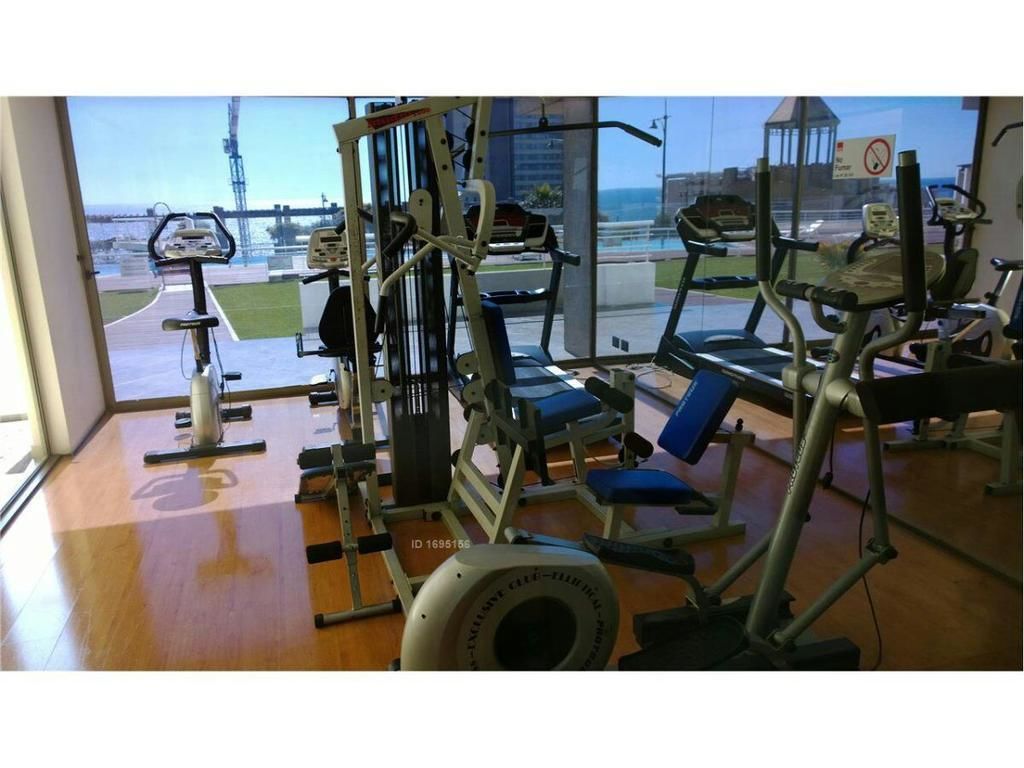 A gym with various exercise equipment, a treadmill, and a view of the outside.