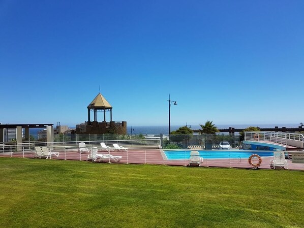 A rooftop pool area with a gazebo, lounge chairs, and a view of the ocean.