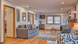 A spacious living room with hardwood flooring, two sofas, a coffee table, and a TV mounted on the wall. - Riverfront Elkins Home w/ Fireplace & Deck! (Elkins)