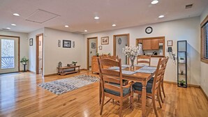 A spacious dining area with wooden furniture, a clock on the wall, and a kitchen in the background. - Riverfront Elkins Home w/ Fireplace & Deck! (Elkins)