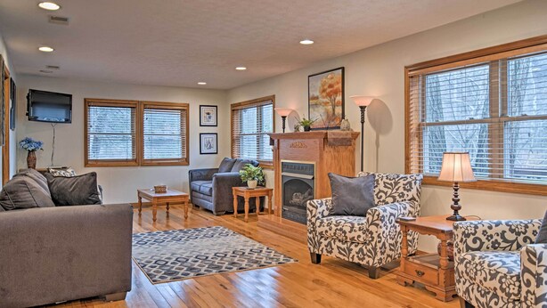 A spacious living room with hardwood flooring, a fireplace, and large windows with blinds. - Riverfront Elkins Home w/ Fireplace & Deck! (Elkins)