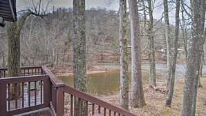 A wooden deck with a railing overlooking a river and forested area. - Riverfront Elkins Home w/ Fireplace & Deck! (Elkins)