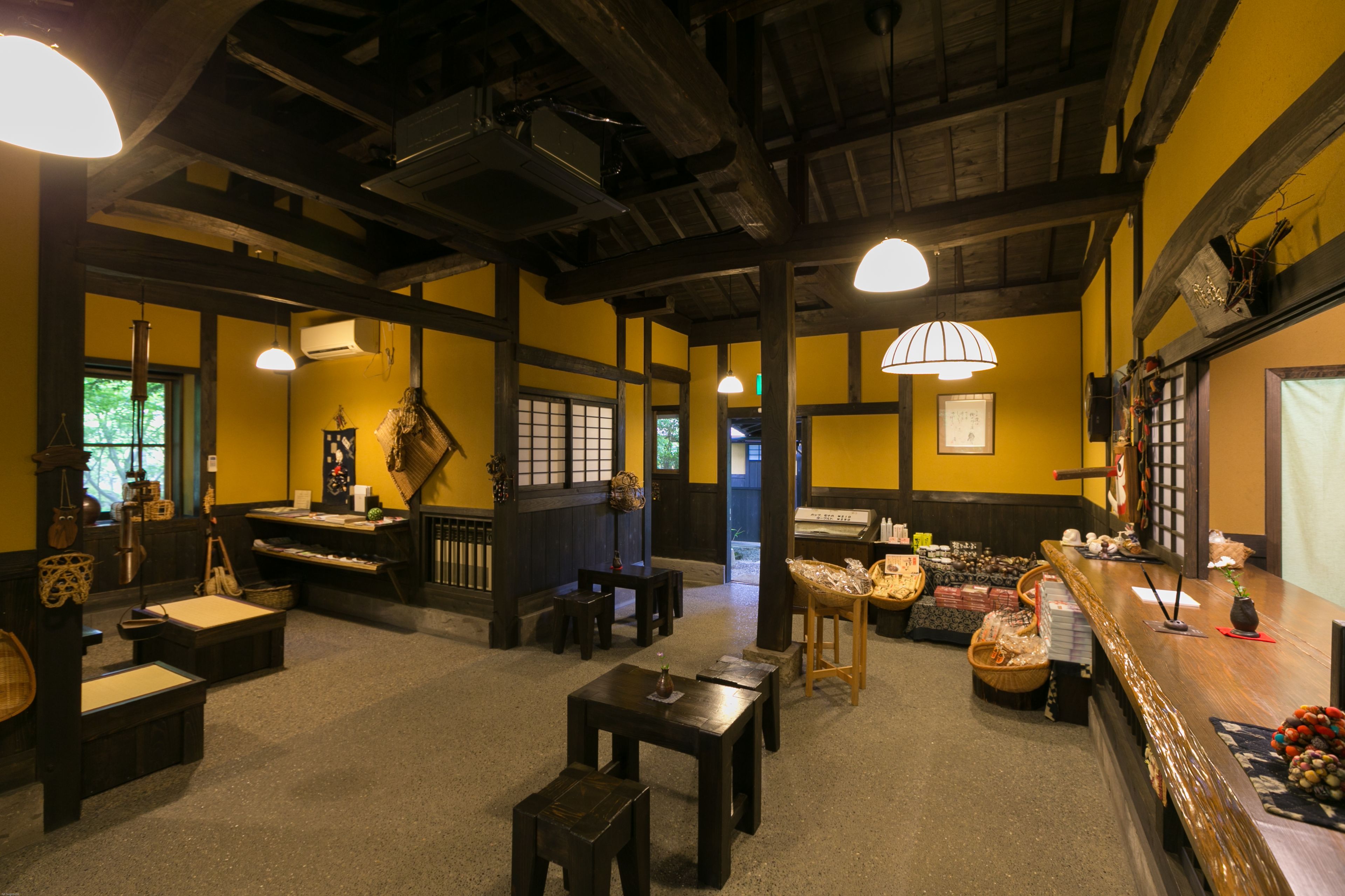 Uma pousada japonesa tradicional com tatames, mobiliário de madeira e uma área de recepção com balcão e diversos serviços.