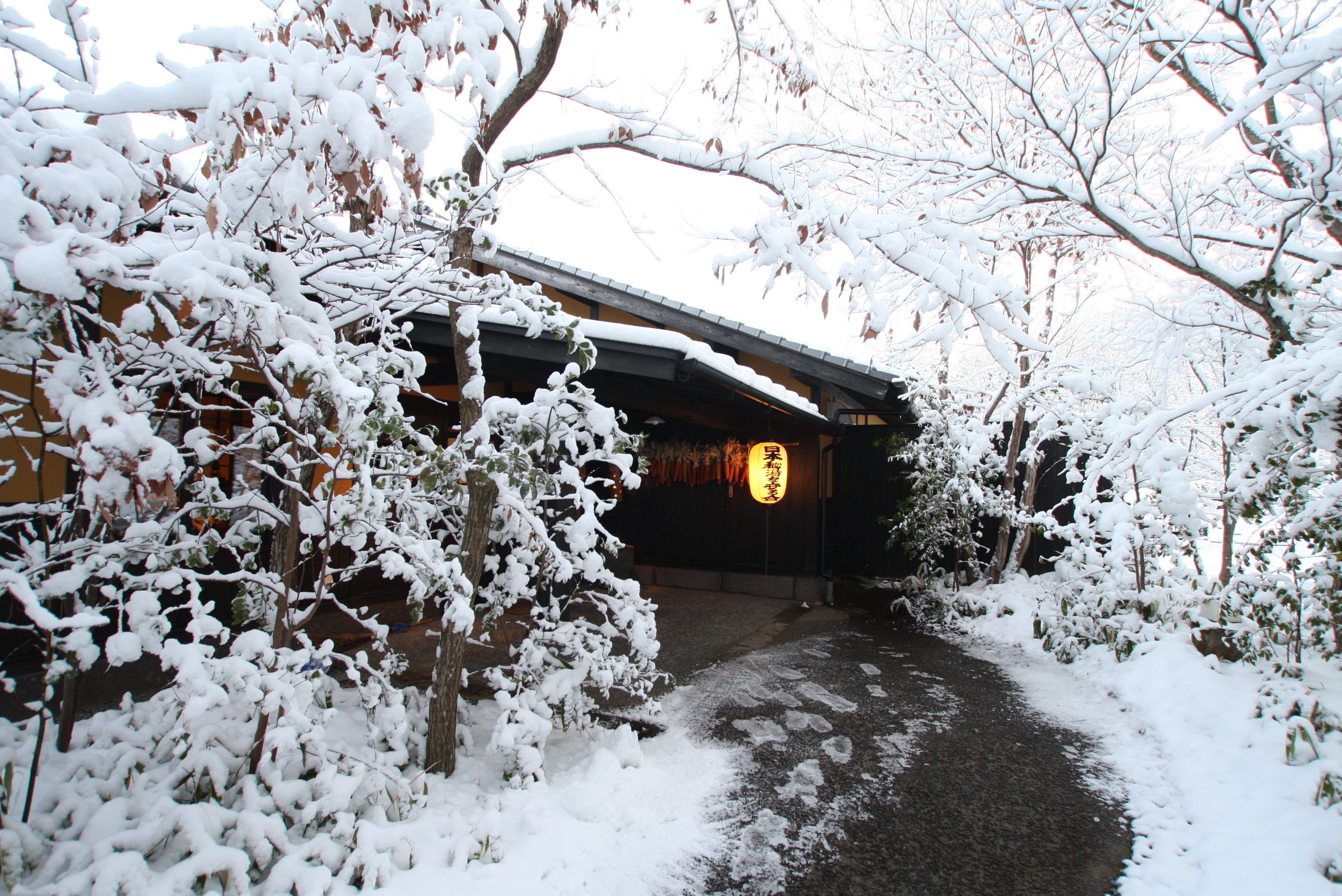 A snow-covered pathway leading to a traditional building with a dark roof and a visible entrance.