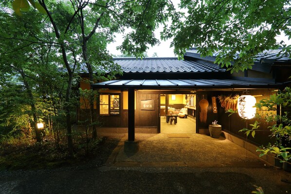 Une maison traditionnelle japonaise, avec un toit recouvert de tuiles, une façade en bois et une entrée bien éclairée.