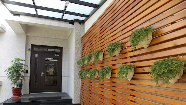 A modern entrance with a black door, a wooden slatted wall with hanging planters, and a small garden area with a potted plant. - Norman's B&B (Hualien City)