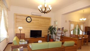 A living room with a sofa, TV, wooden wall paneling, and a chandelier. - Norman's B&B (Hualien City)