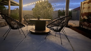 Une terrasse extérieure avec une table ronde et quatre chaises, des guirlandes lumineuses et un arbre.