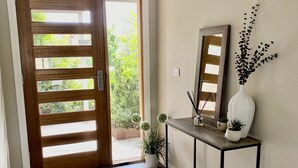 Une porte en bois avec des lattes horizontales, une console avec un miroir et un vase, et une plante en pot.