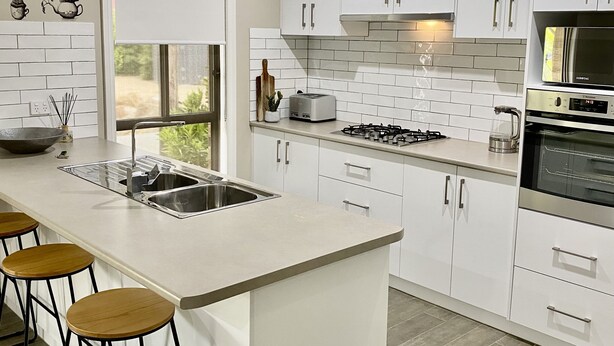 Une cuisine moderne avec des meubles blancs, un îlot central doté de tabourets, une cuisinière à gaz et un four encastré.