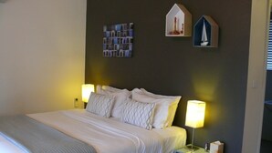 A neatly made bed with white linens and patterned pillows, two bedside lamps, a small shelf with a tissue box, and two wall-mounted decorative items. - Spacious Cottage, overlooking bushland (Pokolbin)