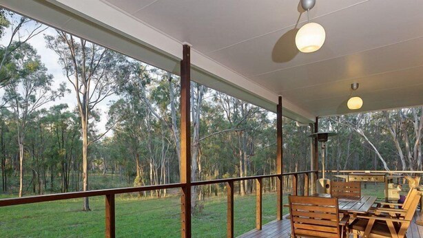 A spacious deck with a wooden table and chairs, overlooking a grassy area with trees. - Spacious Cottage, overlooking bushland (Pokolbin)