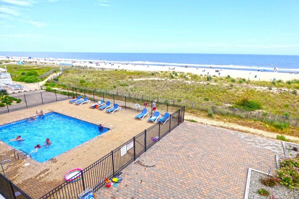 A swimming pool with lounge chairs, a beach view, and a brick patio.