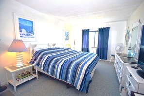A neatly arranged bedroom with a bed, bedside table, lamp, and a desk with a chair.