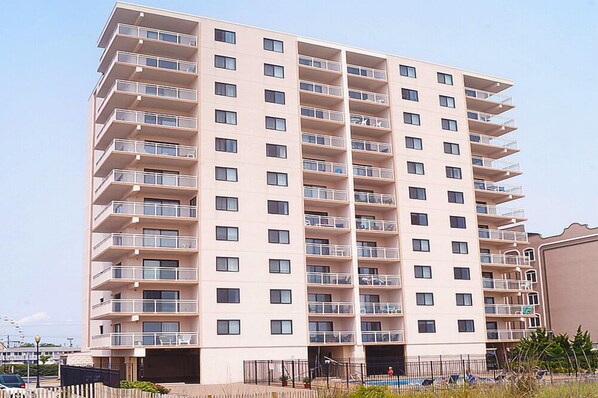A multi-story residential building with balconies, a parking area, and a clear sky. - Towers 201-Oceanfront 29th St, Pool, Elev, W/D, AC, WIFI (Ocean City)