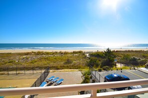 A beach view from a balcony with sun loungers and a parking area.