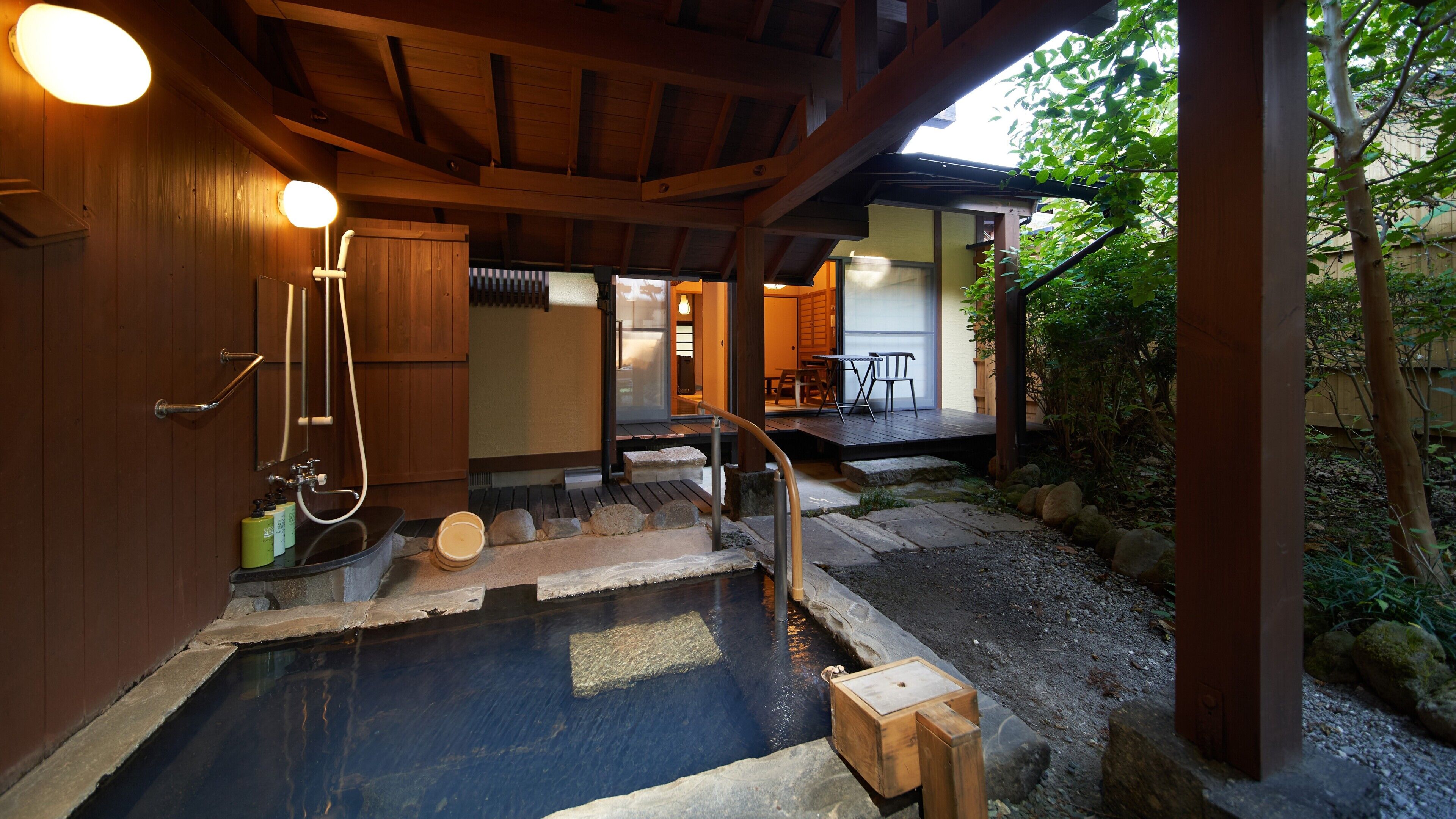 A traditional Japanese onsen with a wooden deck, stone steps, and a wooden bath.