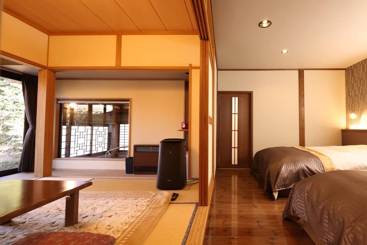 Habitación de hotel con decoración tradicional japonesa, que incluye suelo de tatami, puertas correderas y una cama con cubrecama estampado.