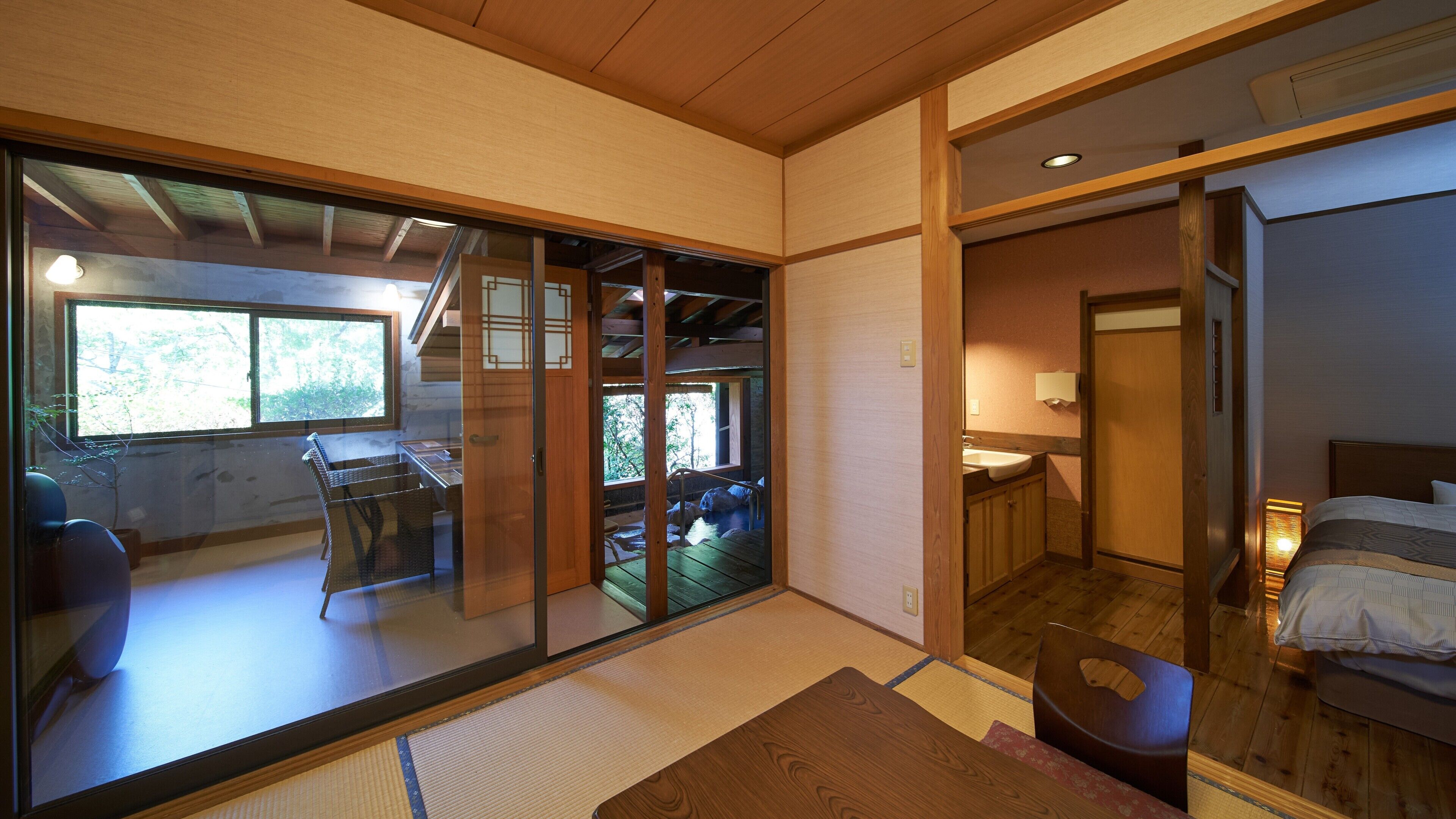 A traditional Japanese-style room with tatami flooring, a sliding door leading to a balcony, a wooden bed, and a small washbasin.