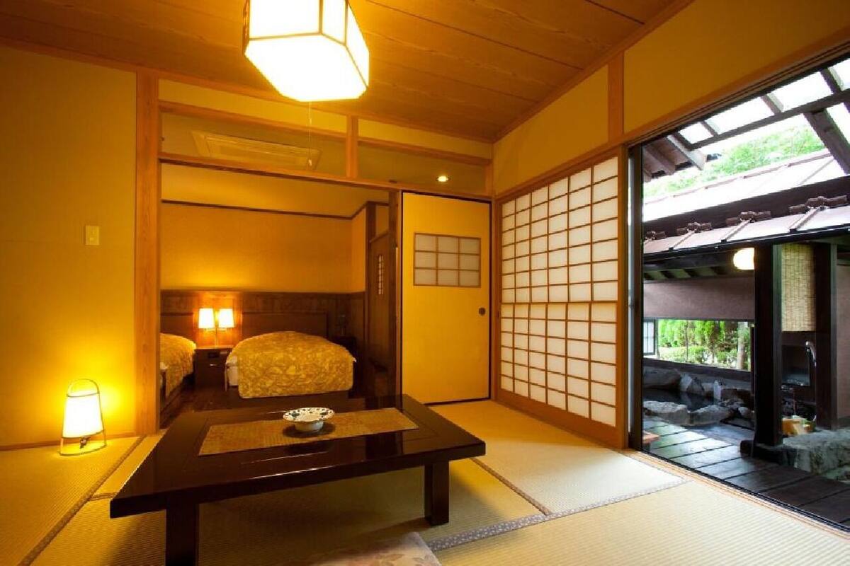 Una habitación japonesa tradicional con suelo de tatami, una mesa baja con un cuenco y puertas correderas que dan a un espacio al aire libre.