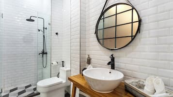 A modern bathroom with a white tiled shower, a white toilet, a wooden vanity with a white sink, and a round mirror.