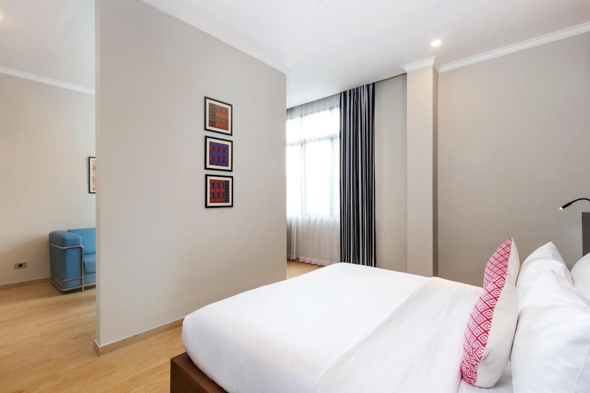 Ett hotellrum med en stor säng, en blå stol och tre inramade tavlor på väggen.