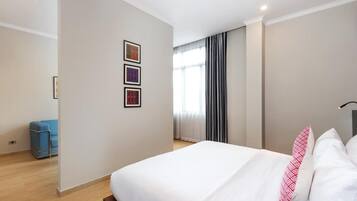 A hotel room with a large bed, a blue chair, and three framed pictures on the wall.