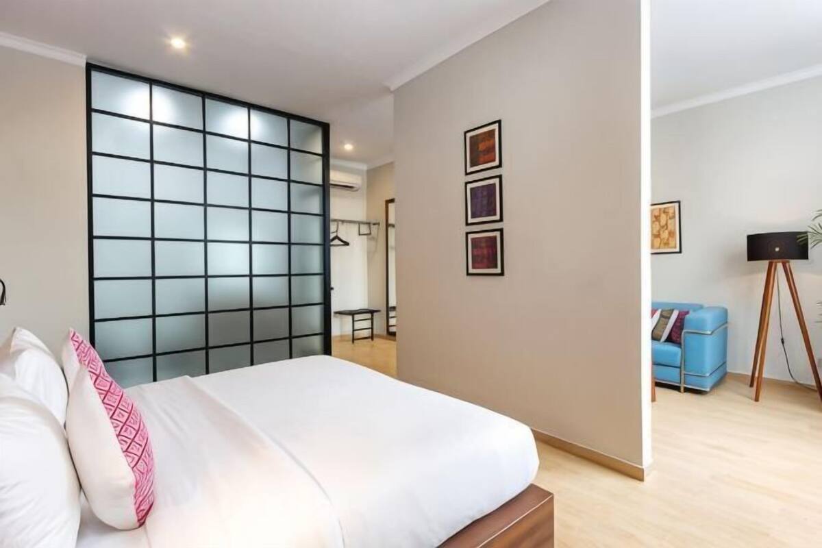 Un dormitorio con cama, puerta corredera, sofá azul y lámpara de pie.