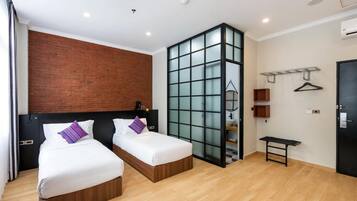 A hotel room with two beds, a brick accent wall, a glass partition, and a small bench.