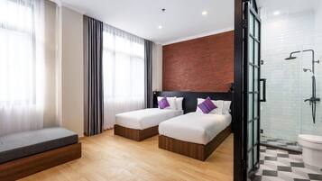 A hotel room with two beds, a bench, a brick accent wall, a glass shower enclosure, and a tiled bathroom.