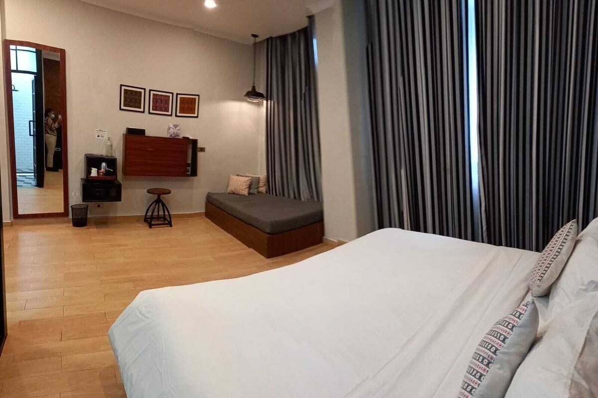 Un dormitorio con una cama grande, una zona de estar pequeña, un escritorio y un espejo.