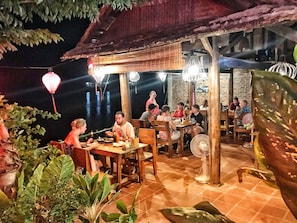 An outdoor dining area with wooden tables and chairs, surrounded by greenery and a view of the water. - Phong Nha Coco House (Phong Nha)
