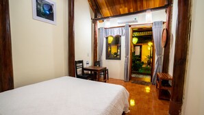 A hotel room with a bed, a wooden table, chairs, and a small desk. There is a door leading to a balcony with plants and a view. - Phong Nha Coco House (Phong Nha)