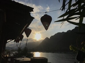 A rustic building with hanging lanterns, a view of a calm lake, and mountains in the background. - Phong Nha Coco House (Bo Trach)