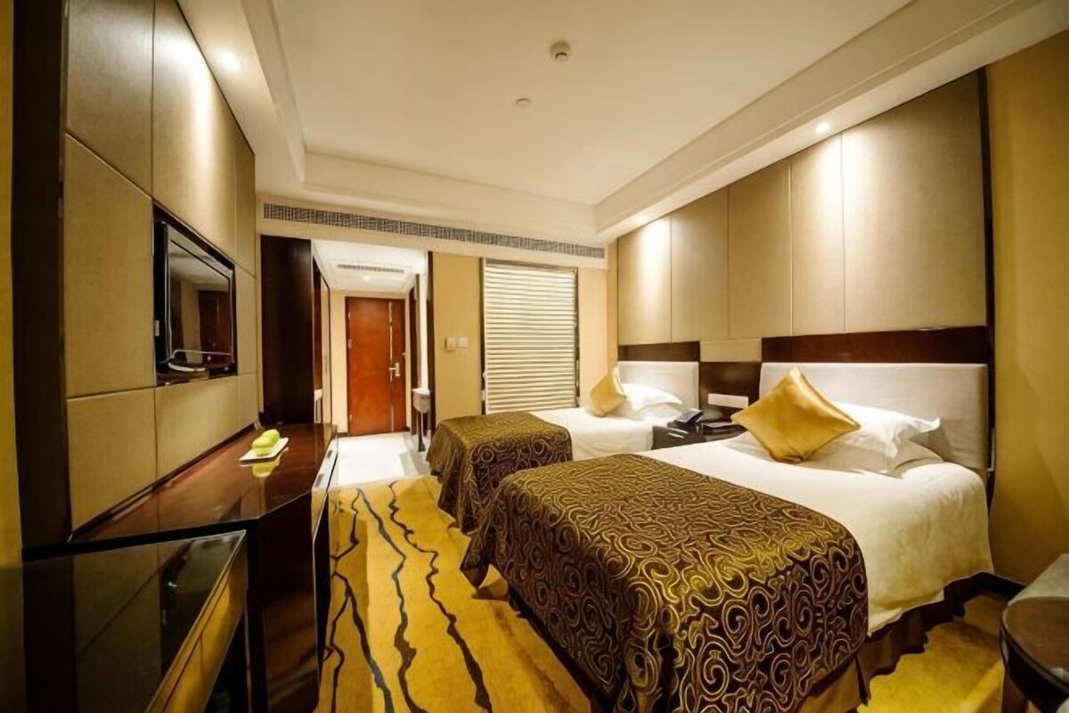 A hotel room with two beds, a TV, a desk, and a mirror.
