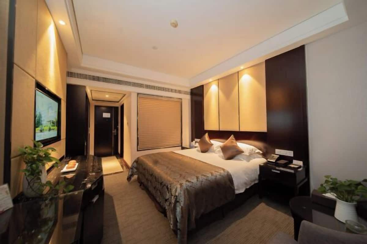 A hotel room with a bed, bedside tables, a TV, and a desk with a chair.