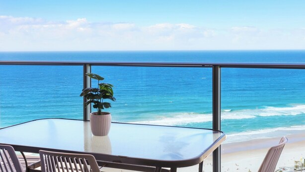 En balkon med et glasbord og stole, der ud til en strand og havet.