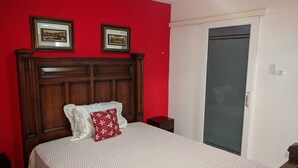 A bedroom with a wooden headboard, a white bedspread with a red pillow, two framed pictures on the wall, and a closed door. - Modern New Kingston Apartment (Secured/Parking) (Kingston)