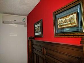 Une pièce avec un mur rouge, une armoire en bois et deux tableaux encadrés.