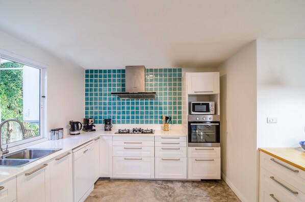 Una cocina compacta con armarios blancos, microondas, horno y cafetera.