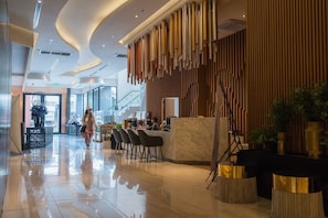 A modern hotel lobby with a marble reception desk, seating area, and a staircase.